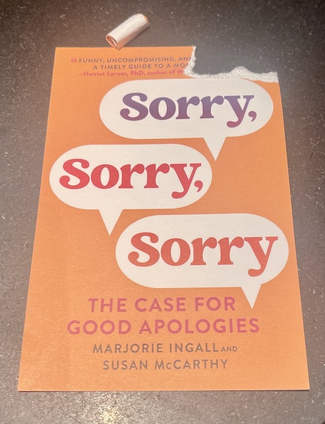 picture of orange notecard depicting book cover, with the text SORRY SORRY SORRY written inside three speech bubbles, in purple, hot pink, and darker orange text. A piece is torn out of the upper right corner and is shown rolled up above the card.
