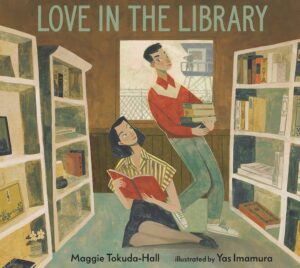 Book cover of "Love in the Library" by Maggie Tokuda-Hall, illustrated by Yas Imamura, depicting a cute Japanese American couple in a library. He's wearing a red button-down shirt with a white yoke, tidy blue jeans, and white sneakers. She's wearing an olive-and-white striped short-sleeve blouse with interesting dropped shoulders and a black skirt and loafers. Their haircuts are from the 1940s. They're surrounded by bookshelves, most with books but there's also a little lamp and a tin can with flowers in it. Through the window behind them, we see wire fencing topped with barbed wire, and a guard tower on which a soldier, in military stance, faces the two young people (and us).