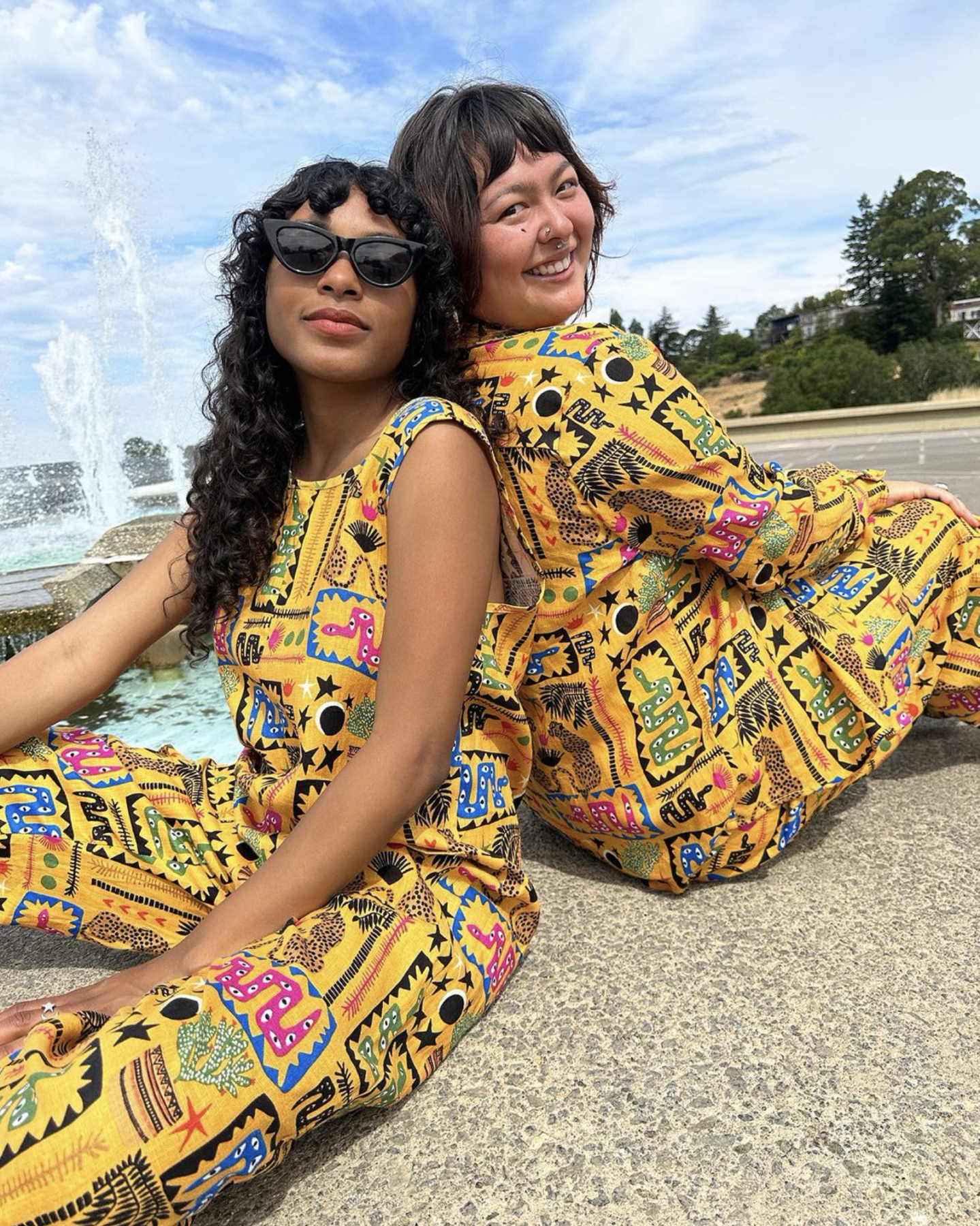 Two models, one straight-size and one plus-sized, pose back to back in Nooworks jumpsuits in the contested yellow print. 