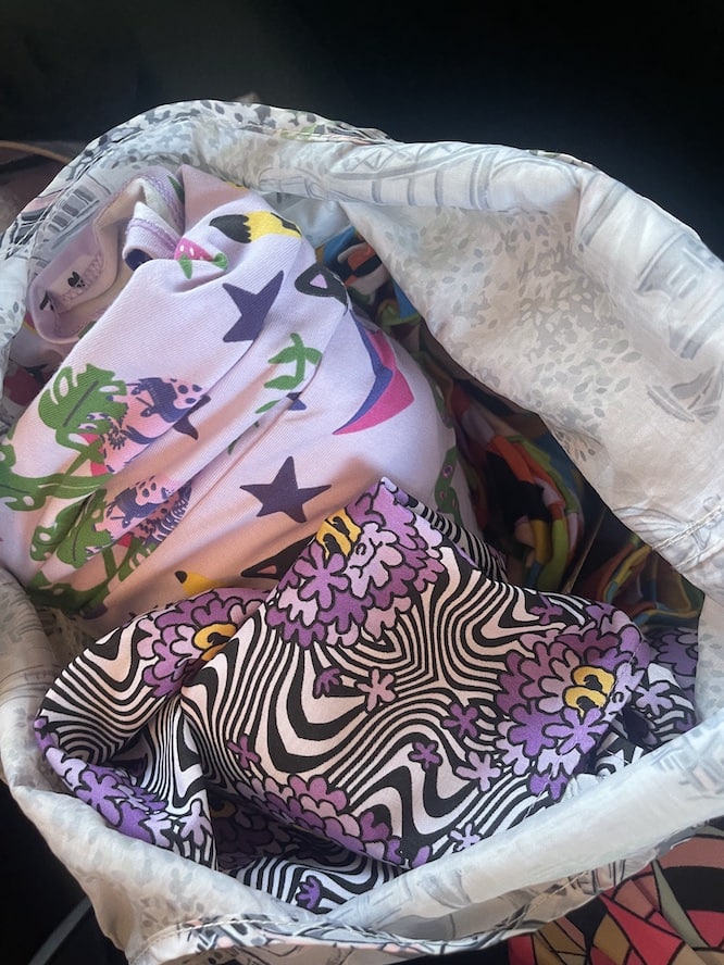 shopping bag containing various Nooworks dresses and shirts in bright patterns