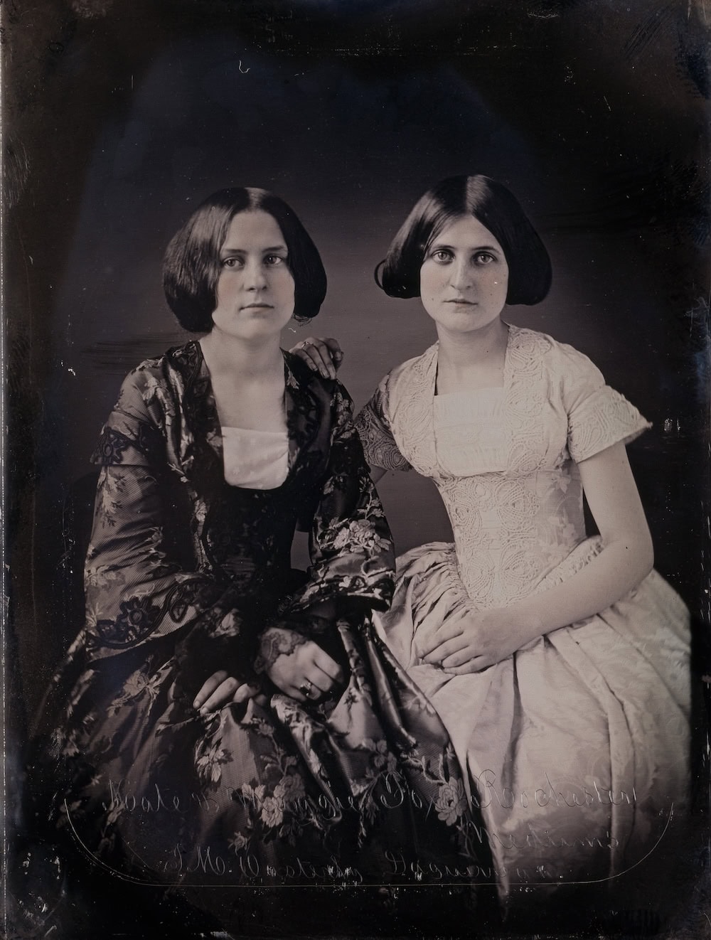 Daguerrotype of young Maggie and Kate Fox, with hands in their laps and straight hair parted in the middle and curled under at the ends, both looking somberly at the viewer